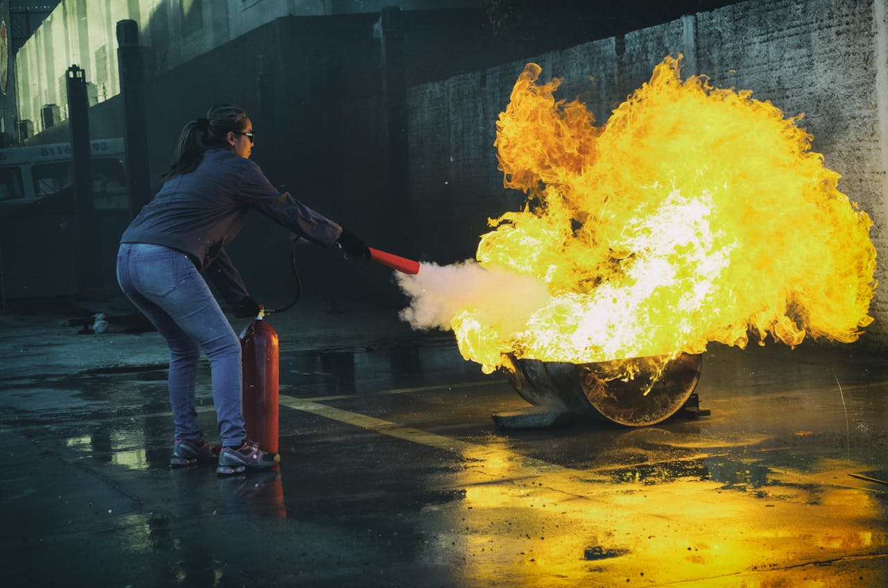 A woman uses a fire extinguisher to put out a large flame in an outdoor setting, showcasing fire safety.